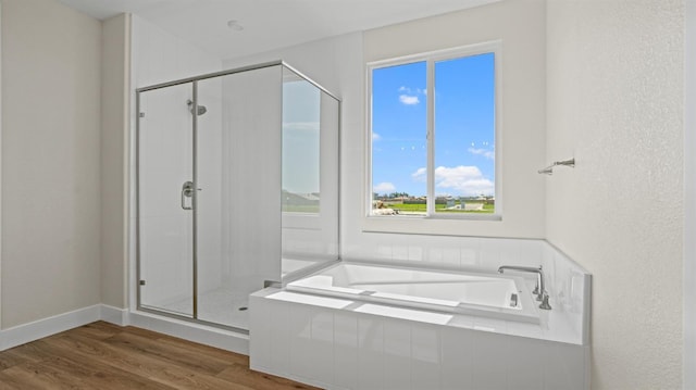 bathroom with baseboards, a shower stall, a bath, and wood finished floors