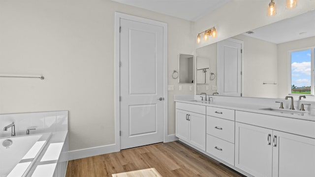 full bathroom with double vanity, a sink, wood finished floors, a freestanding tub, and baseboards