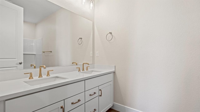 full bath featuring double vanity, a shower, a sink, and baseboards