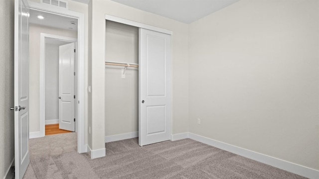 unfurnished bedroom featuring a closet, visible vents, light carpet, and baseboards