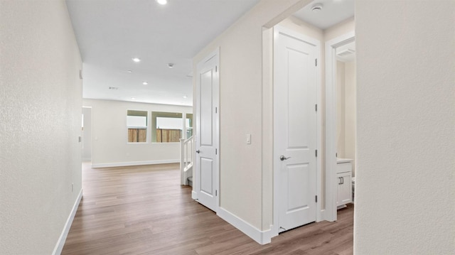 hall with light wood-style floors, recessed lighting, a textured wall, and baseboards