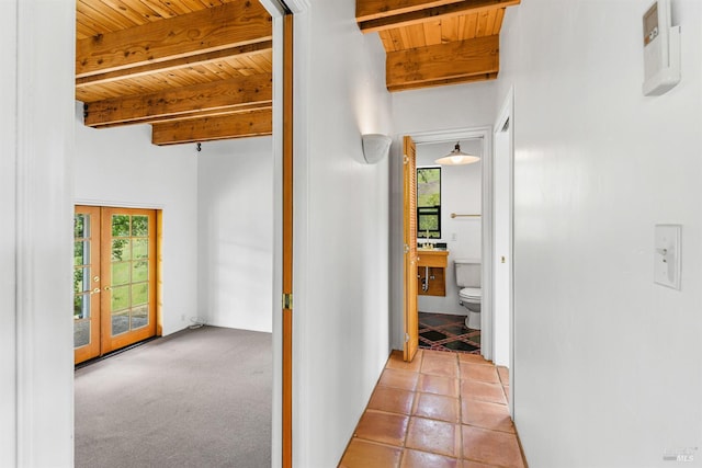 corridor featuring beamed ceiling, light carpet, wood ceiling, and french doors