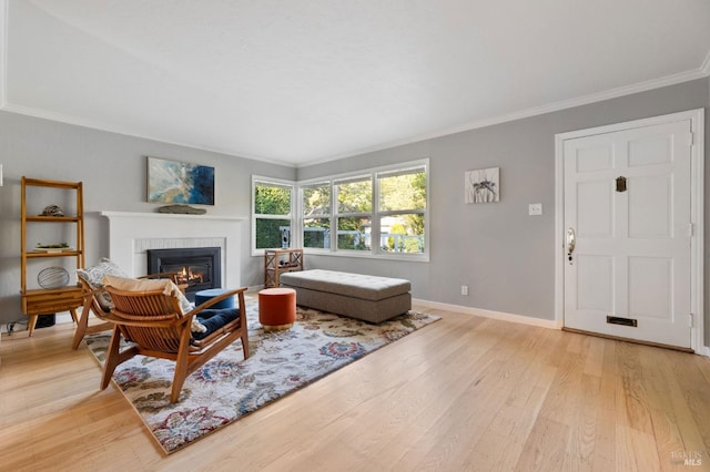 living room featuring light wood finished floors, a glass covered fireplace, baseboards, and ornamental molding