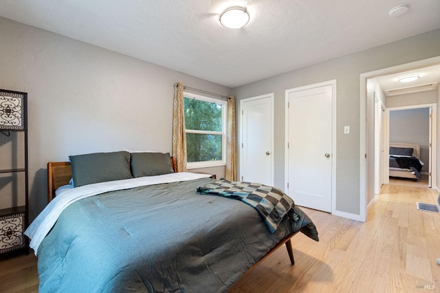 bedroom with attic access, baseboards, light wood-style floors, and multiple closets