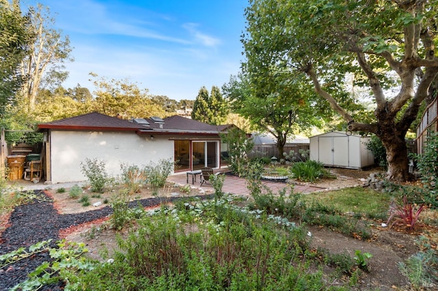 rear view of property with an outbuilding, a patio, fence, stucco siding, and a storage shed