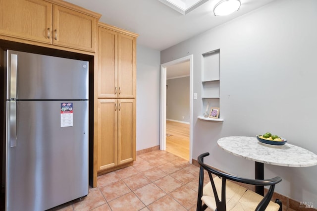 kitchen featuring light brown cabinetry, freestanding refrigerator, light countertops, light tile patterned floors, and baseboards