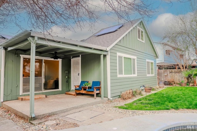 rear view of property with ceiling fan, a patio, fence, a yard, and board and batten siding