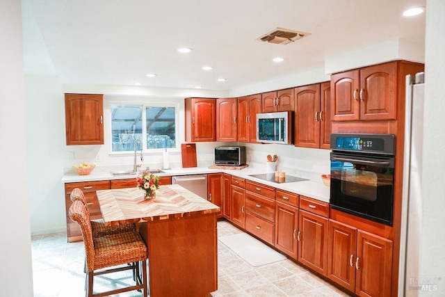 kitchen with recessed lighting, a sink, visible vents, black appliances, and a kitchen bar