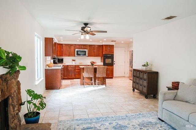 kitchen with a center island, stainless steel microwave, visible vents, open floor plan, and black oven