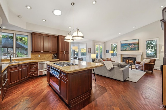 kitchen with sink, hanging light fixtures, dark hardwood / wood-style floors, light stone countertops, and a kitchen island