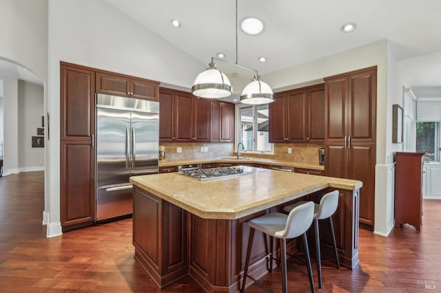 kitchen featuring lofted ceiling, sink, stainless steel appliances, a kitchen island, and decorative light fixtures