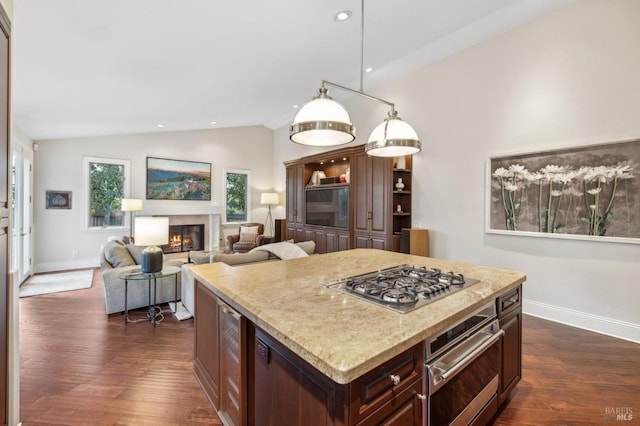 kitchen with vaulted ceiling, appliances with stainless steel finishes, a kitchen island, dark hardwood / wood-style flooring, and hanging light fixtures