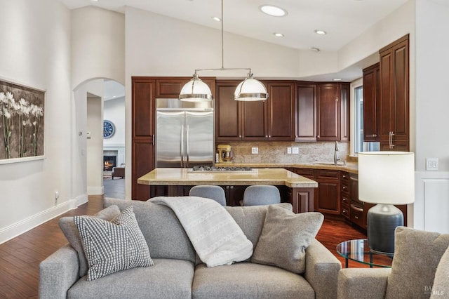 kitchen with dark wood-type flooring, light stone counters, a center island, pendant lighting, and stainless steel appliances