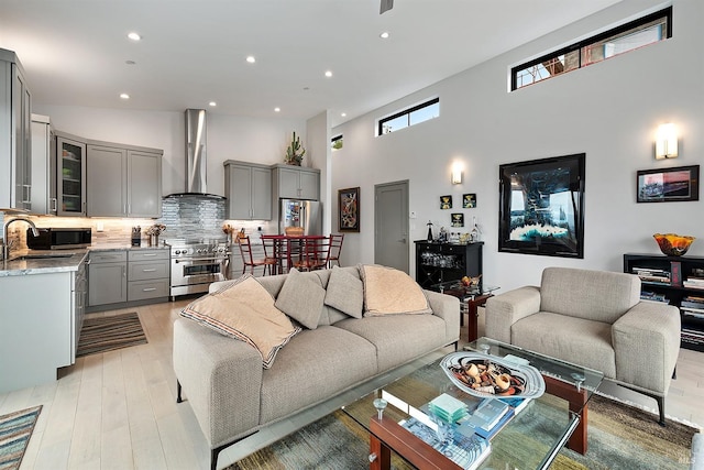 living room with sink, light wood-type flooring, and a towering ceiling