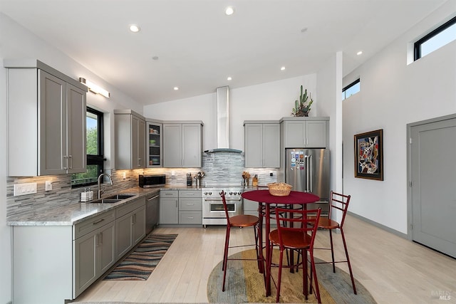 kitchen with wall chimney exhaust hood, sink, light stone counters, premium appliances, and gray cabinets