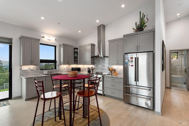 kitchen with gray cabinetry, high end appliances, light stone countertops, light hardwood / wood-style floors, and wall chimney exhaust hood