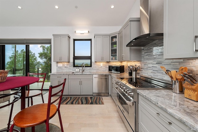 kitchen featuring sink, gray cabinets, appliances with stainless steel finishes, light stone counters, and wall chimney exhaust hood