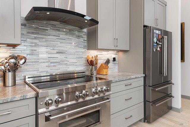 kitchen with gray cabinetry, high end appliances, tasteful backsplash, light stone countertops, and range hood