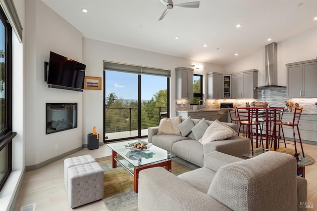 living room featuring ceiling fan, lofted ceiling, sink, and light hardwood / wood-style flooring