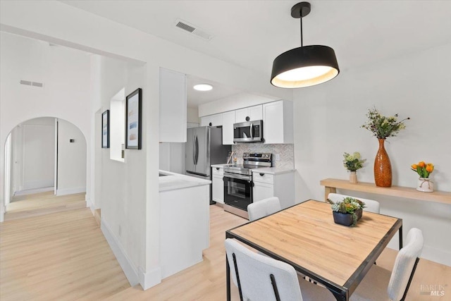 kitchen with stainless steel appliances, white cabinetry, light hardwood / wood-style floors, and decorative backsplash