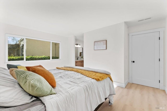 bedroom featuring connected bathroom and light hardwood / wood-style floors