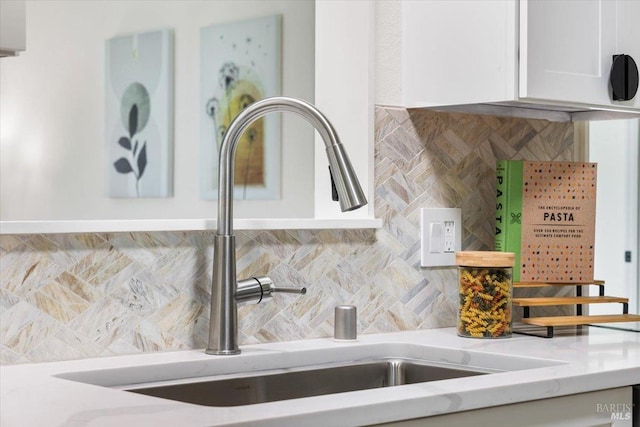 details featuring sink, white cabinets, light stone counters, and decorative backsplash