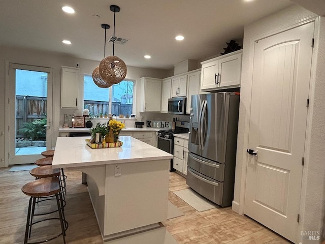 kitchen with appliances with stainless steel finishes, white cabinetry, a kitchen breakfast bar, hanging light fixtures, and a center island