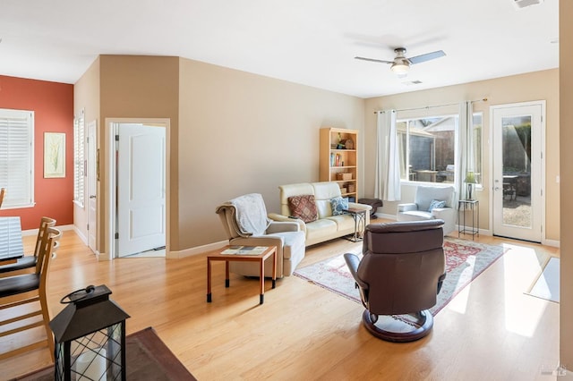 living room featuring a ceiling fan, visible vents, light wood-style floors, and baseboards