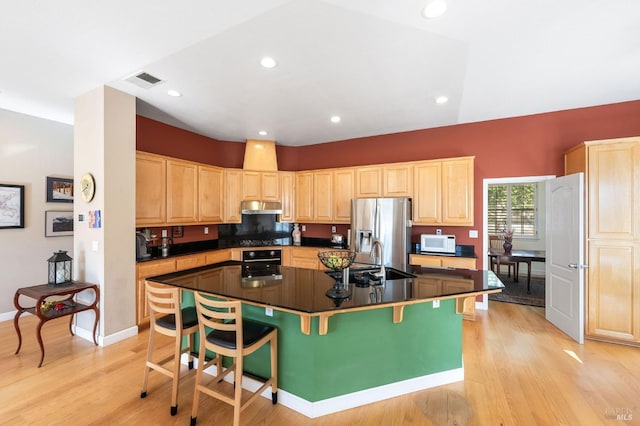 kitchen with oven, stainless steel fridge with ice dispenser, under cabinet range hood, and light brown cabinetry