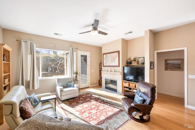 living area featuring visible vents, baseboards, a glass covered fireplace, and wood finished floors