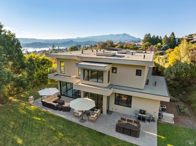 rear view of property featuring a lawn, outdoor lounge area, a patio area, a mountain view, and a balcony