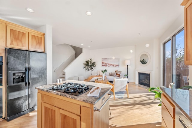 kitchen featuring black fridge with ice dispenser, gas stovetop, dark stone countertops, a kitchen island, and light hardwood / wood-style floors