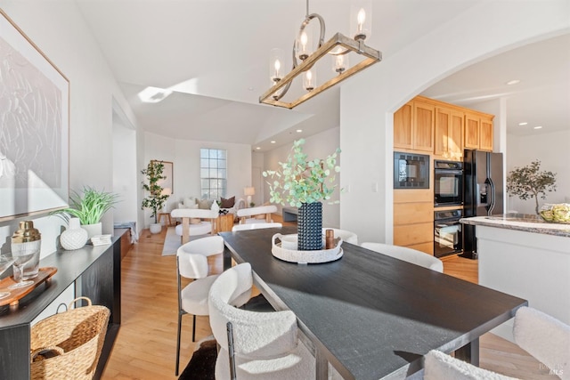 dining room with an inviting chandelier, vaulted ceiling, and light wood-type flooring