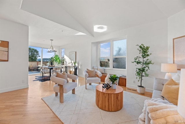 living room featuring lofted ceiling, a wealth of natural light, a notable chandelier, and light hardwood / wood-style floors