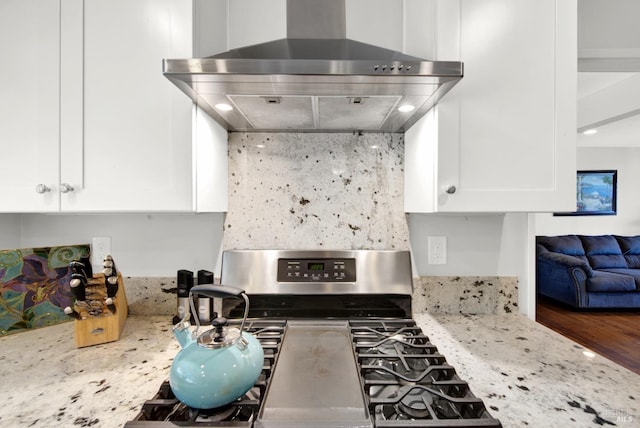 kitchen featuring light stone counters, wall chimney range hood, stainless steel gas range oven, and white cabinets