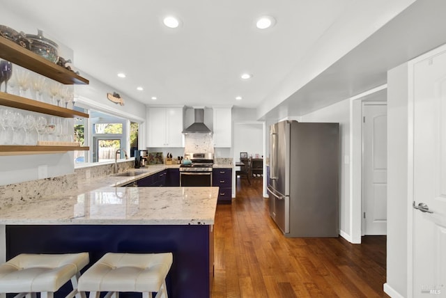 kitchen featuring appliances with stainless steel finishes, sink, white cabinets, kitchen peninsula, and wall chimney range hood