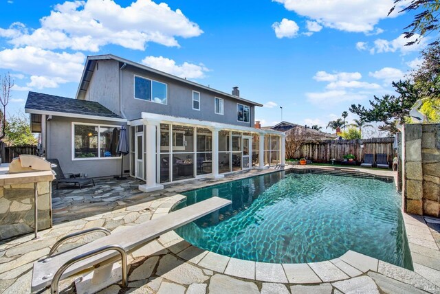 rear view of property featuring a fenced in pool, a sunroom, a patio, and an outdoor kitchen