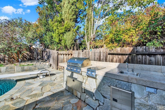 view of patio with area for grilling, a grill, sink, and a fenced in pool