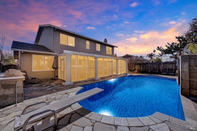 pool at dusk featuring a patio, an outdoor kitchen, and a diving board