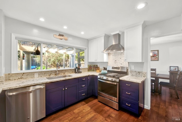 kitchen with blue cabinetry, sink, white cabinetry, stainless steel appliances, and wall chimney range hood