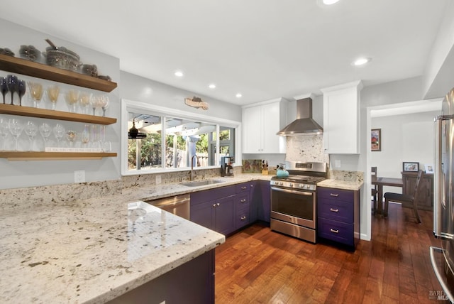 kitchen with sink, white cabinets, light stone counters, stainless steel appliances, and wall chimney range hood