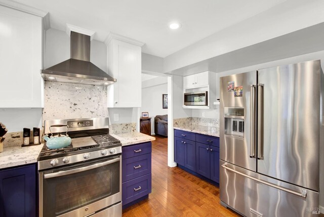 kitchen featuring blue cabinets, extractor fan, appliances with stainless steel finishes, light stone countertops, and white cabinets