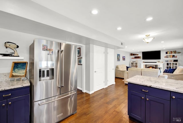 kitchen featuring light stone counters, blue cabinetry, high end fridge, and dark wood-type flooring