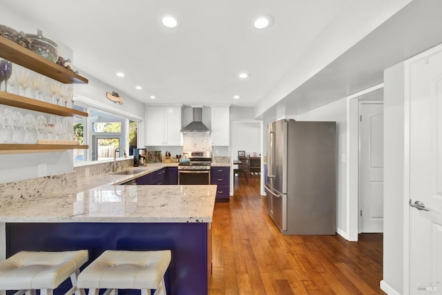 kitchen featuring wall chimney range hood, sink, white cabinetry, stainless steel appliances, and kitchen peninsula