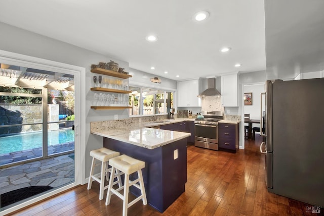 kitchen with appliances with stainless steel finishes, a breakfast bar, white cabinetry, sink, and wall chimney exhaust hood