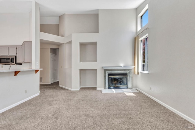 unfurnished living room featuring sink, light carpet, and high vaulted ceiling