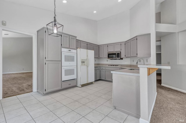 kitchen featuring high vaulted ceiling, hanging light fixtures, light colored carpet, kitchen peninsula, and white appliances