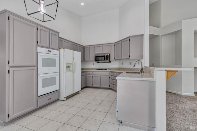 kitchen featuring sink, gray cabinetry, kitchen peninsula, a towering ceiling, and white appliances