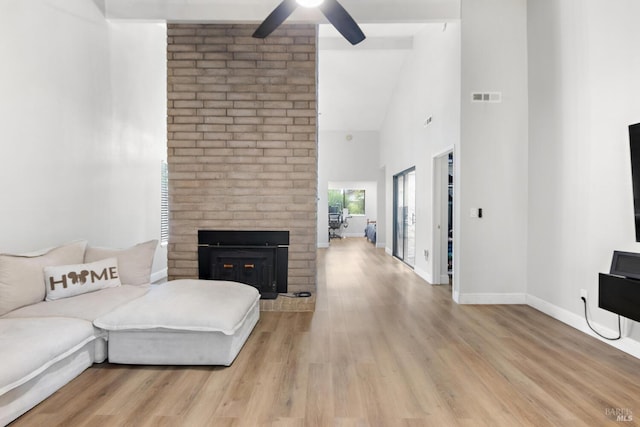 living room with a brick fireplace, high vaulted ceiling, ceiling fan, and light wood-type flooring