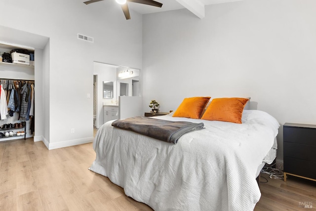 bedroom featuring ensuite bathroom, a high ceiling, light hardwood / wood-style floors, beam ceiling, and a closet